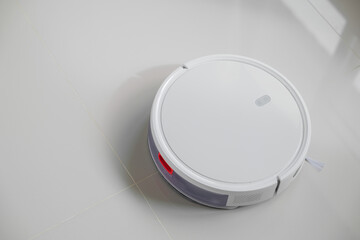White automatic floor cleaner with side brush on tile flooring, designed for efficient cleaning....