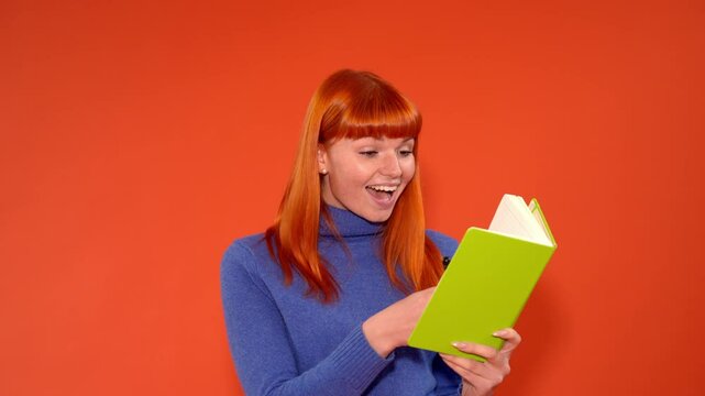 Woman with orange hair smiles while writing in a green notebook against a bright orange background, showcasing creativity and joy during a personal reflection moment