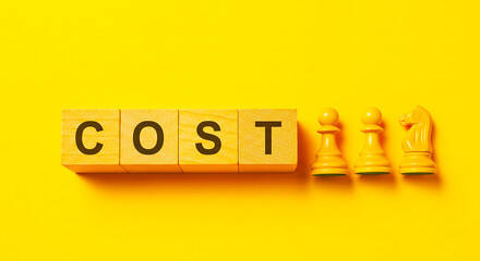 Cost spelled out in wooden blocks with chess pieces on a bright yellow colored background studio shot
