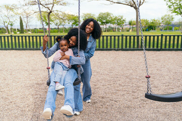 Mother and aunt joyfully pushing their niece on a swing in a vibrant playground, creating cherished...