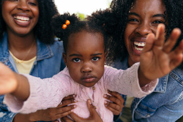 Mother and aunt joyfully embracing niece, sharing laughter and warmth on a sunny day in the park,...