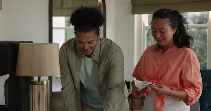 Diverse couple sorting baby clothes on bed in softly lit bedroom, celebrating baby kick by kneeling