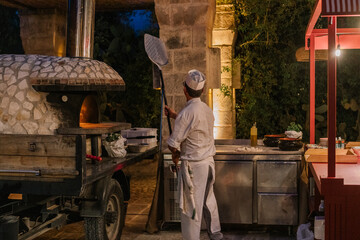 Italian pizzaiolo placing a freshly prepared pizza into a traditional wood-fired oven.