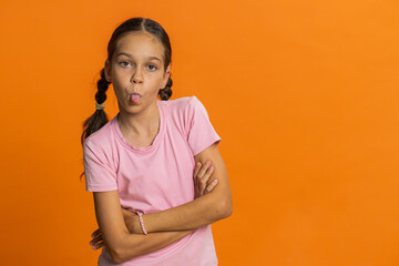 Cheerful funny young school girl showing tongue making faces at camera, fooling around, joking,...