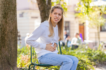 Sick ill young woman suffering from period cramps painful stomach ache outdoors. Girl teenager...