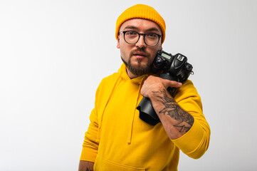 Emotional, smiling young man in yellow hoodie and cap holding camera in studio. Hipster...