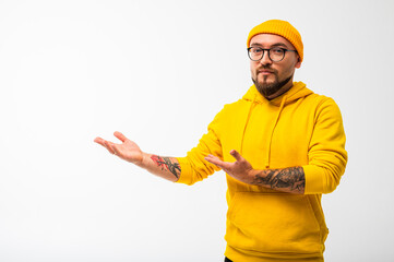 Confident bearded man in yellow hoodie and beanie pointing sideways with serious face. Isolated on...