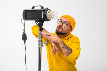Portrait of a young man in yellow hoodie and beanie posing with a studio light against white background. Photographer concept, creative professional look