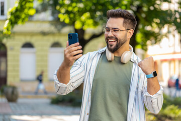 Excited amazed Caucasian man outside using mobile phone device winning online shocked male tourist...