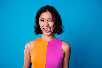 Young woman with a playful expression against a vibrant blue background wearing a colorful top and...