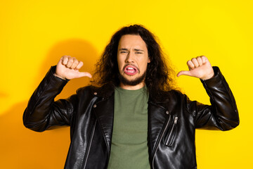 Young man with long black hair wearing a leather jacket expressing disapproval on vibrant yellow...