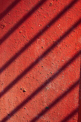 Concrete painted red with a shadow from a fence. Rustic background