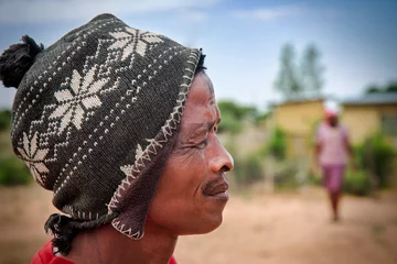 Fototapeten village rural ,portrait of african man profile view , in front of a house, countryside living, he is wearing a beanie with motifs © poco_bw
