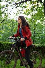 Beauty smiling woman in sport black cap biking on bicycle on spring trees background. Sporty wear...