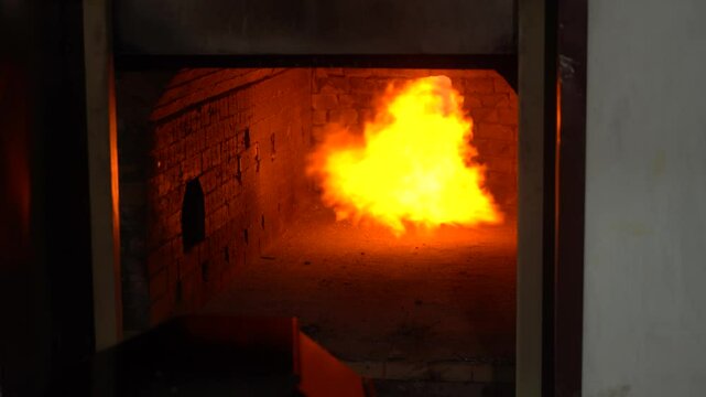 The crematorium door opens, and a fire burns inside.