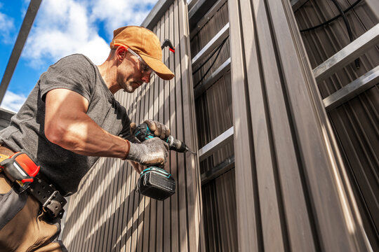 Construction Worker Installing Lamella Composite Panels on a Building During a Sunny Day in a Suburban Area
