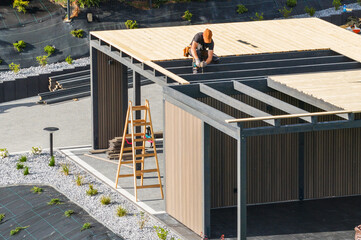 Construction Worker Installing Wooden Beams on a Modern Building Structure in a Suburban Area