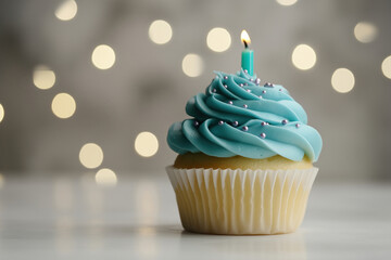 Delicious cupcake with teal frosting and a single candle on a white surface, bokeh background