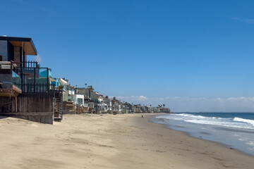 Beach house on stilts near water edge at Carbon-La Costa Beach in Malibu, California, USA against blue sky