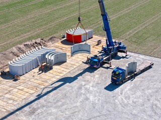 Turmsegmente werden von einem Kran auf eine Baustelle für eine Windkraftanlage abgesetzt,...