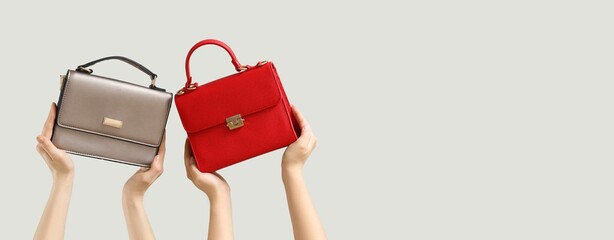 Female hands holding stylish women's bags on light background with space for text