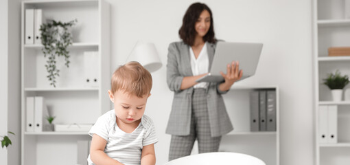 Fototapeta premium Cute little baby playing with cubes on desk while mother working in office