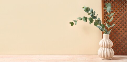 Vase with green eucalyptus branches on beige background with space for text