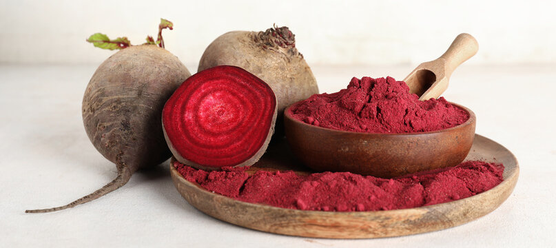 Wooden plate of vibrant beetroot powder with scoop, bowl and fresh beets on white background
