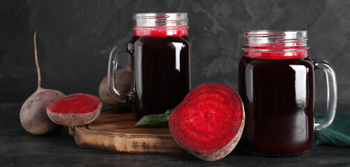 Mason jars of fresh beet juice with basil and vegetables on black background