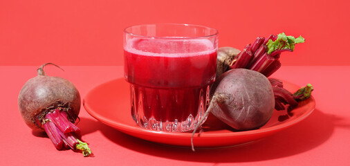 Plate with glass of healthy beet juice on red background