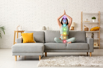 Pretty young woman doing breath practice on sofa at home