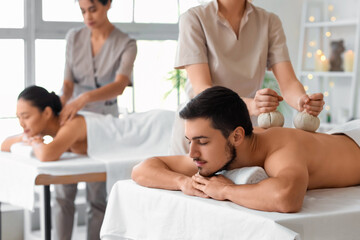 Fototapeta premium Young man getting massage with herbal bags in spa salon