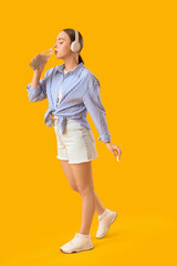 Young woman in headphones drinking chia seed water on yellow background