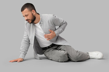 Young man suffering from heart attack on floor on grey background