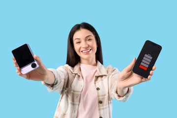 Beautiful young woman with modern power bank and discharged mobile phone on blue background