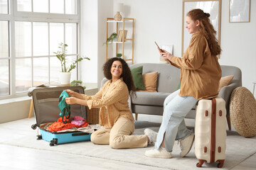 Beautiful young happy female friends packing suitcases at home