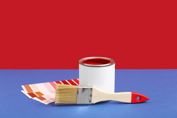 Can of red paint with brush and color palettes on colorful background