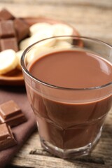 Tasty chocolate milk, pieces and banana on wooden table, closeup