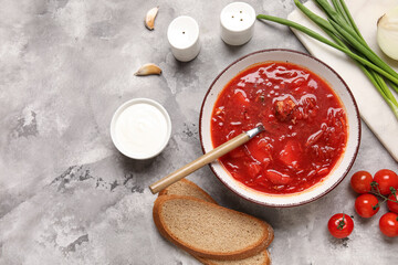 Bowl of tasty Ukrainian borscht and ingredients on grey background