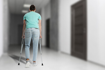 Man with axillary crutches in hospital, back view. Space for text