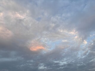 The expansive sky is dominated by soft, layered cloud formations, featuring varying shades of gray,...