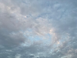 The expansive sky is dominated by soft, layered cloud formations, featuring varying shades of gray,...