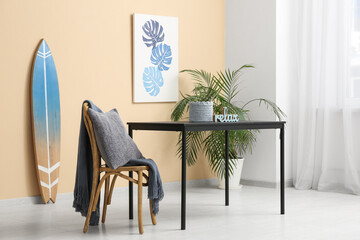 Interior of stylish room with table, chair, houseplant and surfboard