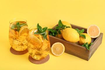 Glasses of lemon ice tea with mint and citrus fruits on yellow background