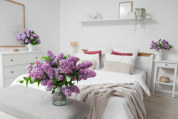 Interior of light bedroom with lilac flowers in vases