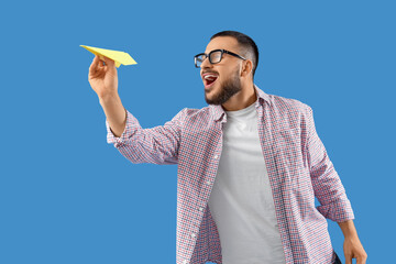 Young man with paper plane on blue background