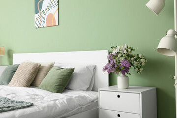 Vase with beautiful flowers on bedside table near green wall in bedroom, closeup