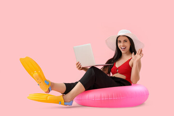 Young businesswoman with laptop, swimming ring and flippers on pink background. Concept of vacation