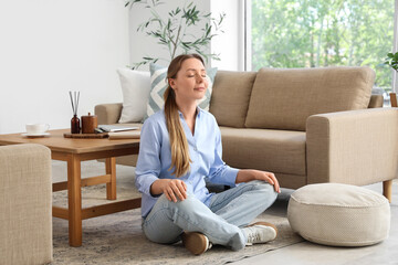 Calm young woman meditating near grey sofa in living room