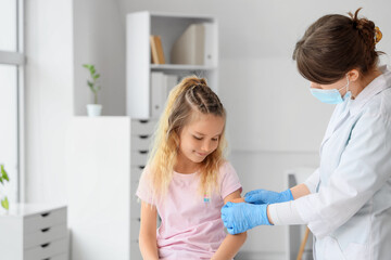 Fototapeta premium Cute little girl receiving patch from doctor after vaccination in clinic